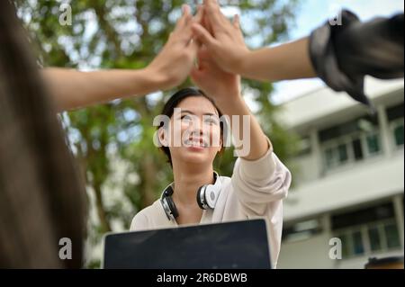 A close-up image of a pretty young Asian female college student giving high fives with her friends outdoors. Team support, Teamwork, Relationship, Fri Stock Photo
