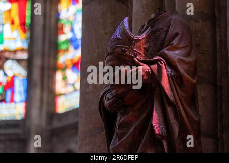 Statue of St. Denis of France holding his own head. Sculpture is bathed in colored light from the stained glass windows of St. Denis Basilica Stock Photo