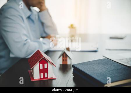 Real estate broker agent presenting and consult to customer to decision making sign insurance form agreement, home model, concerning mortgage loan off Stock Photo