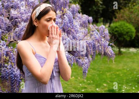 Girl with nose allergy sneezing. Polen illnes symptom concept. Woman allergic to blossom during spring blooming tree outdoor. Stock Photo