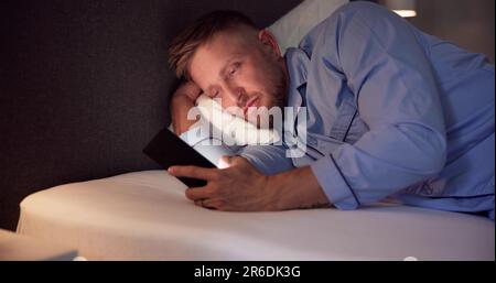 Man Lying On Bed Using Mobile Phone At Night Stock Photo