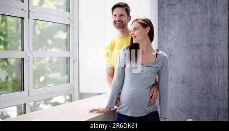 Portrait Of Happy Young Pregnant Couple Near Window Stock Photo