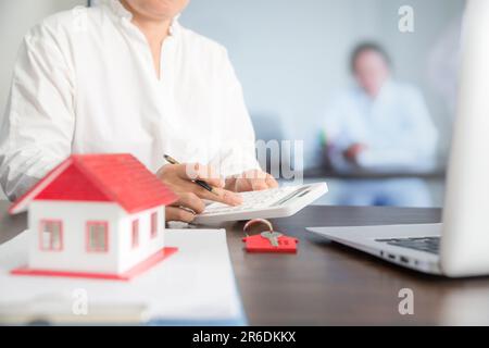 Small house model on wooden table and professional financial advisor is using calculator. Stock Photo