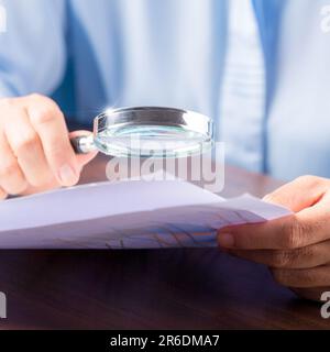 professional business woman hand holding and using magnifying glass search finance document paper on desk in office, businesswoman looking at data wit Stock Photo