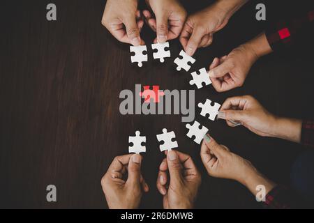 High Angle View Of Businesspeople Hand Solving Jigsaw Puzzle On Wooden Desk Stock Photo