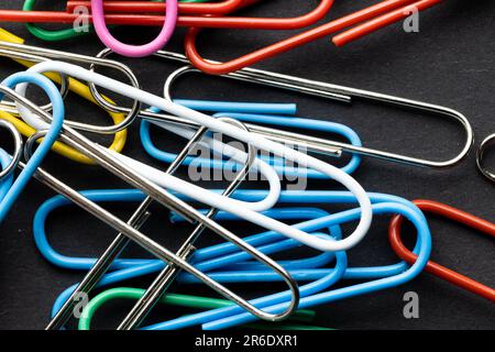 Close up of close up of multi coloured paper clips on black background. School materials, organising, learning, school and education concept. Stock Photo