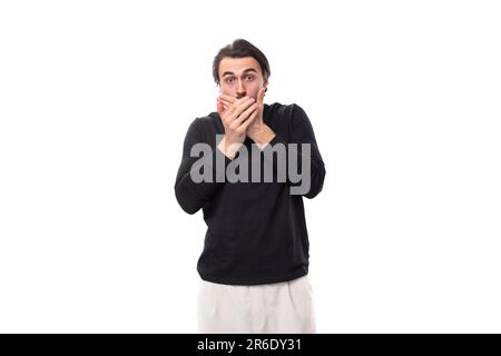 portrait of a well built young man with black hair and beard dressed in a black jacket covering his mouth with his hand isolated on a white background Stock Photo