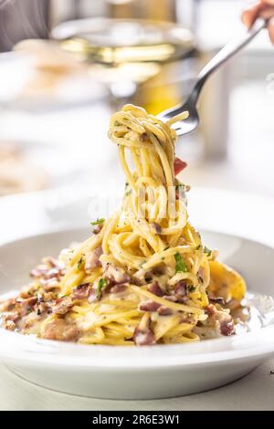 Detail of a fork spinning spaghetti carbonara from a full plate. Stock Photo