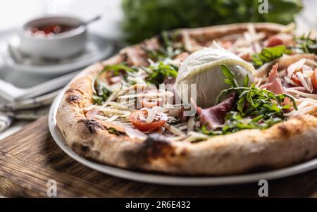 Ham, ruccola, tomatoes and cheese pizza with entire mozzarella di bufala Campana on top. Stock Photo