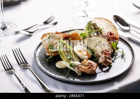 A twist of an elegant ceasar salad with shrimps served on a dark plate in a restaurant. Stock Photo
