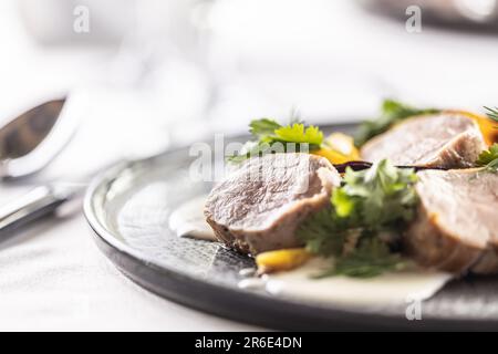 Detail of pork medallions with vegetables and dressing on a shallow dark plate. Stock Photo