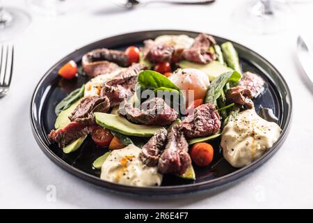 Colorful salad with flank steak filling the dark plate on a restaurant table. Stock Photo