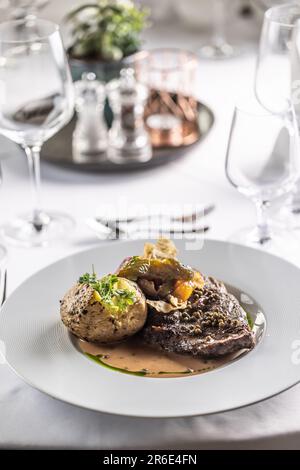 Ribeye steak with green pepper sauce and baked whole potato presented on a nicely decorated table. Stock Photo