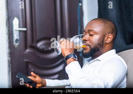 young adult african businessman with beards having refreshment from wineglass while using mobile phone. Technology Stock Photo