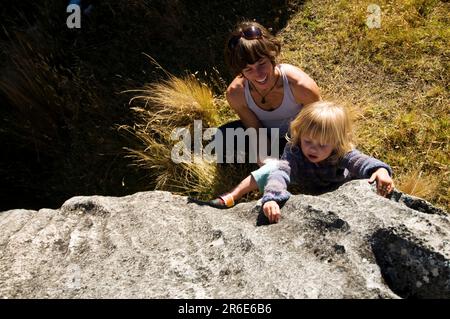 A mother encourages her young daughter to climb a limestone boulder in Castle Hill, New Zealand. Stock Photo