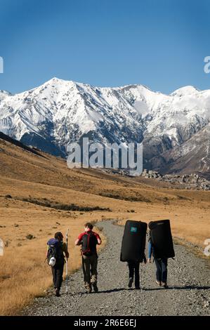 Rock climbers walk a farm road out to limestone boulders in the Castle Hill Basin, New Zealand. Stock Photo