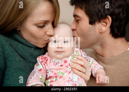 Parents kiss their baby in a family portrait for a christmas Card. Stock Photo