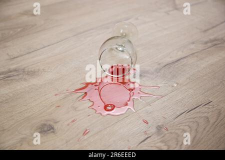 Glass of red wine fell on laminate, wine spilled on floor. Stock Photo