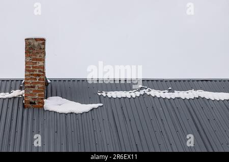 a brick chimney on a metal roof in the winter under the snow. construction concept. Stock Photo