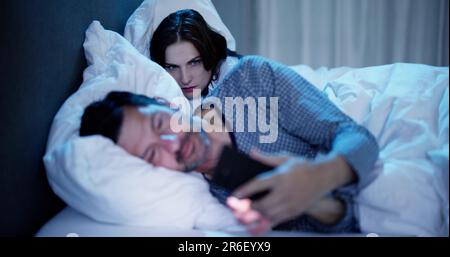 Woman Looking At Man Talking On Mobile Phone In Bedroom Stock Photo