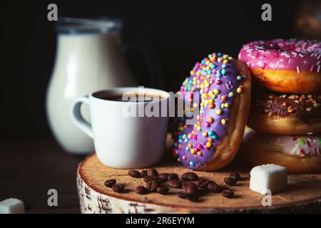 Stack of assorted donuts, a jug of milk and a cup of coffee on a dark background. Stock Photo