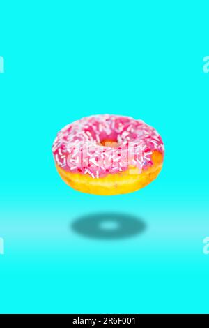 Flying donut with pink icing on a turquoise background. Stock Photo