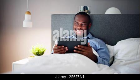 Man Lying On Bed Looking At Illuminated Digital Tablet Stock Photo