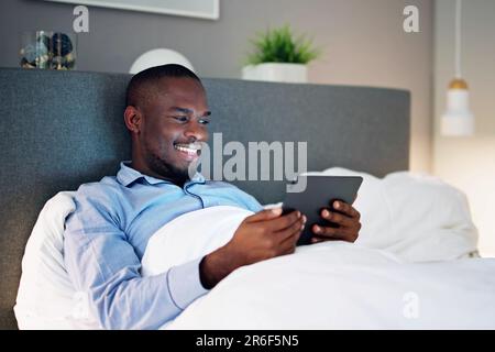 Man Lying On Bed Looking At Illuminated Digital Tablet Stock Photo