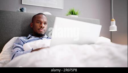 Happy Man Sitting On Bed Using Laptop Stock Photo