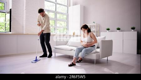 Man Helping Pregnant Wife. Cleaning House. Young Couple Stock Photo