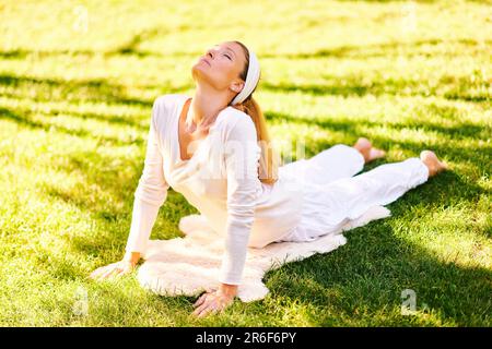 Beautiful healthy woman practicing yoga in summer park or garden, urdhva mukha svanasana or upward-facing dog pose Stock Photo