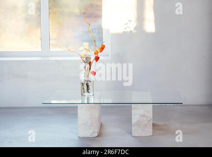 Minimalist modern light interior with coffee table and window. Magazin table with glass top and stone supports. Transparent glass vase with bouquet of Stock Photo