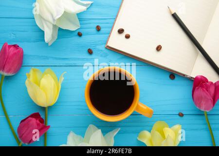 Notebook with cup of coffee and tulips on blue background. Top view Stock Photo