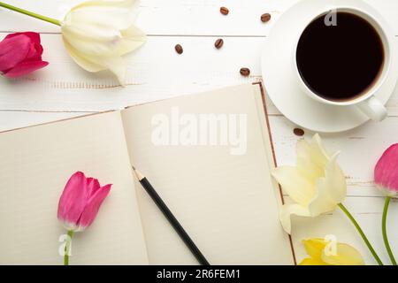 Notebook with cup of coffee and tulips on light background. Top view Stock Photo