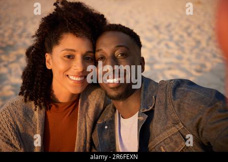 Smiling young multiethnic couple taking a selfie on a sandy beach Stock Photo