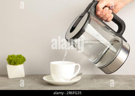 https://l450v.alamy.com/450v/2r6fg35/kettle-pouring-boiling-water-into-a-cup-on-grey-background-top-view-2r6fg35.jpg