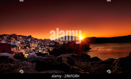 The glorious sun setting behind a quaint village by the sea Stock Photo