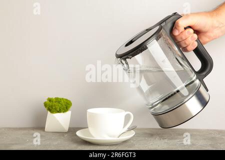 https://l450v.alamy.com/450v/2r6fgt3/kettle-pouring-boiling-water-into-a-cup-on-grey-background-top-view-2r6fgt3.jpg