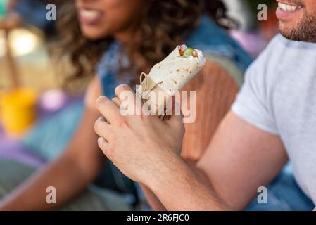 man is holding a vegan burrito in his hand beside a woman having good time-no faces Stock Photo