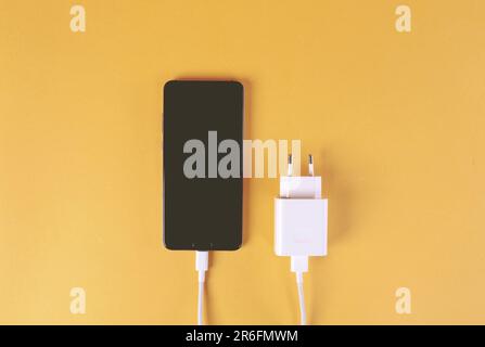 A mobile phone connected to an electrical socket and wired together with a charging cable Stock Photo