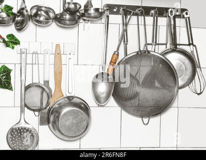 A white wall with a variety of cookware hung on it, including pans, pots and utensils Stock Photo