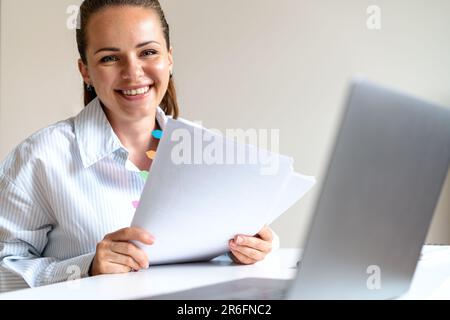 Portrait of young woman economist with financial documents in her hands, looking at camera and smiling. Stock Photo