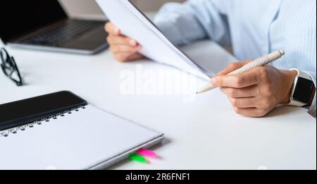 Office worker sitting at the desk holding pen and documents in hands, doing paperwork . Stock Photo