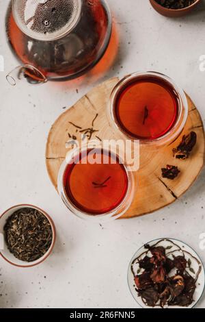 Different types of tea. Black, green and hibiscus sorts on a white table with teapot and glasses. Stock Photo