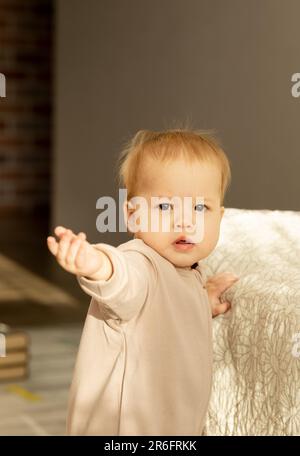 Asian baby reaches out and looks into the camera, leaning on the bed Stock Photo