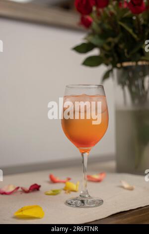 An alcoholic drink served in a glass, on the table with rose petals and a bouquet in the background Stock Photo