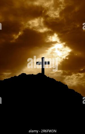 Silhouette of a cross on top of a mountain at sunset. With the suns rays shining down on the cross Stock Photo
