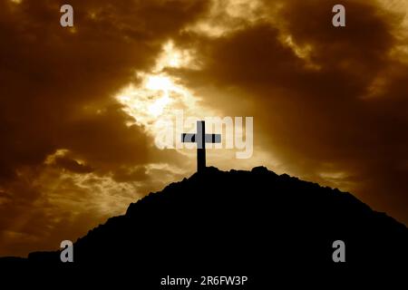 Silhouette of a cross on top of a mountain at sunset. With the suns rays shining down on the cross Stock Photo