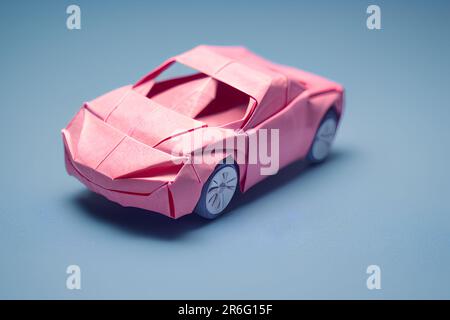 A miniature pink model origami car displayed on a bright blue ...