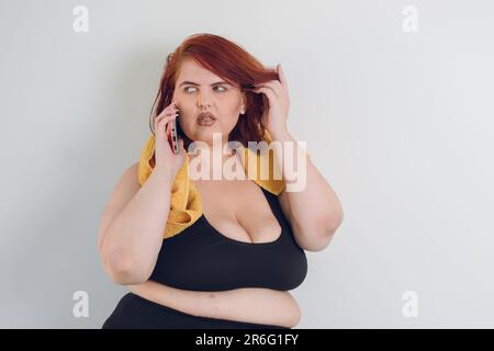 young sporty plus size argentinian latin woman standing talking on the phone over white background, copy space, technology concept, black sportswear, Stock Photo